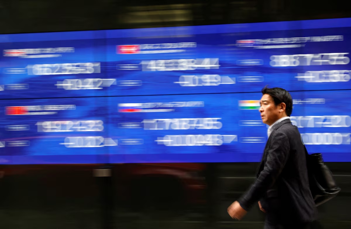 一名路人走过东京一家银行外的电子显示屏，显示屏上显示着各国股票价格指数 ...