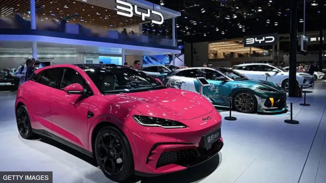 BYD汽车展销现场，三台分别为玫红色、萤光绿、银白色的车并列